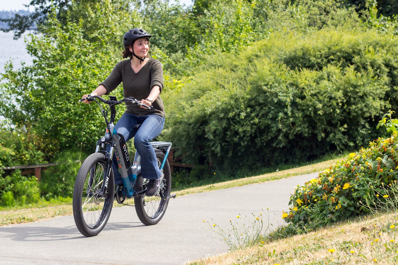 heros-img Woman biking on a scenic path in Seattle, showcasing modern electric bike and lifestyle.